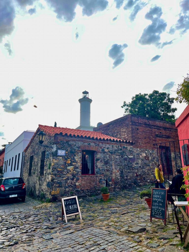 A cobblestone street lined with colorful colonial buildings in Colonia del Sacramento, Uruguay, with vintage cars parked along the side