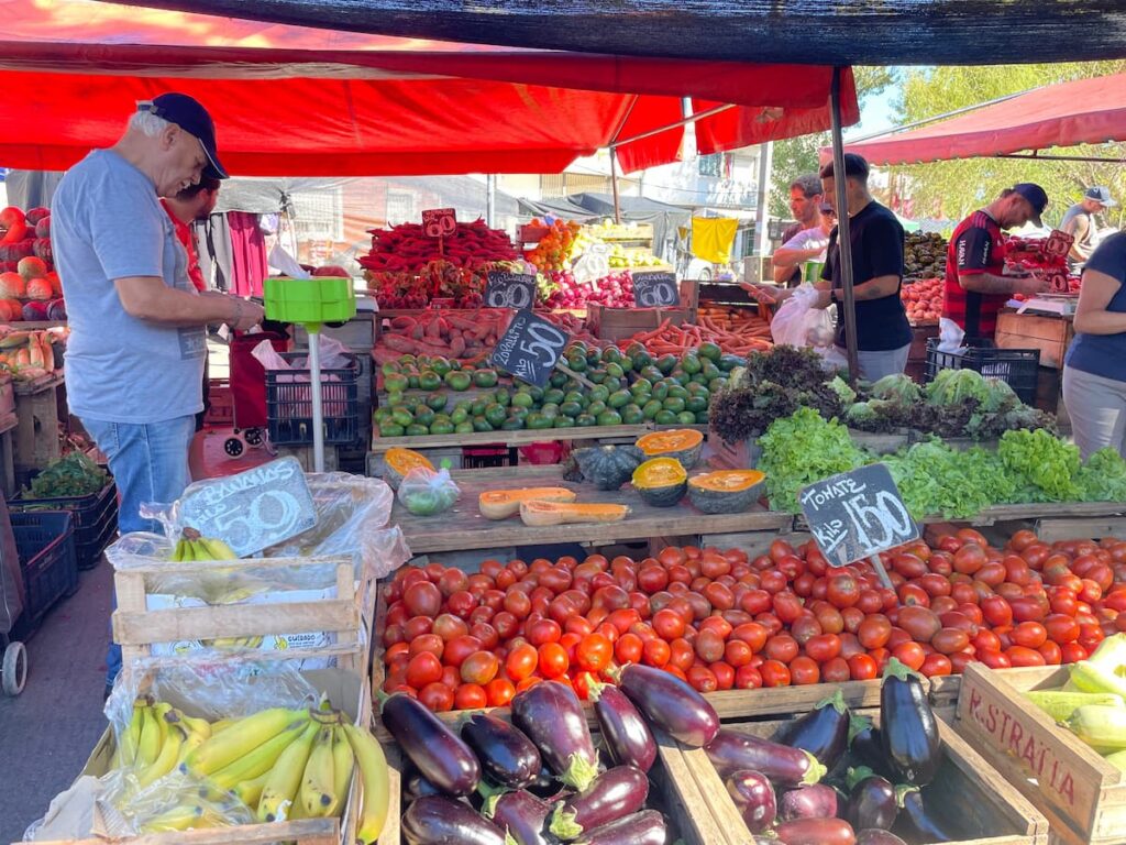 Colorful assortment of fresh fruits and vegetables in wooden crates outdoor Uruguayan farmer's market displaying tomatoes, eggplant, bananas, lettuce, squash, carrots, sweet potatoes, and zucchini, food quality in uruguay