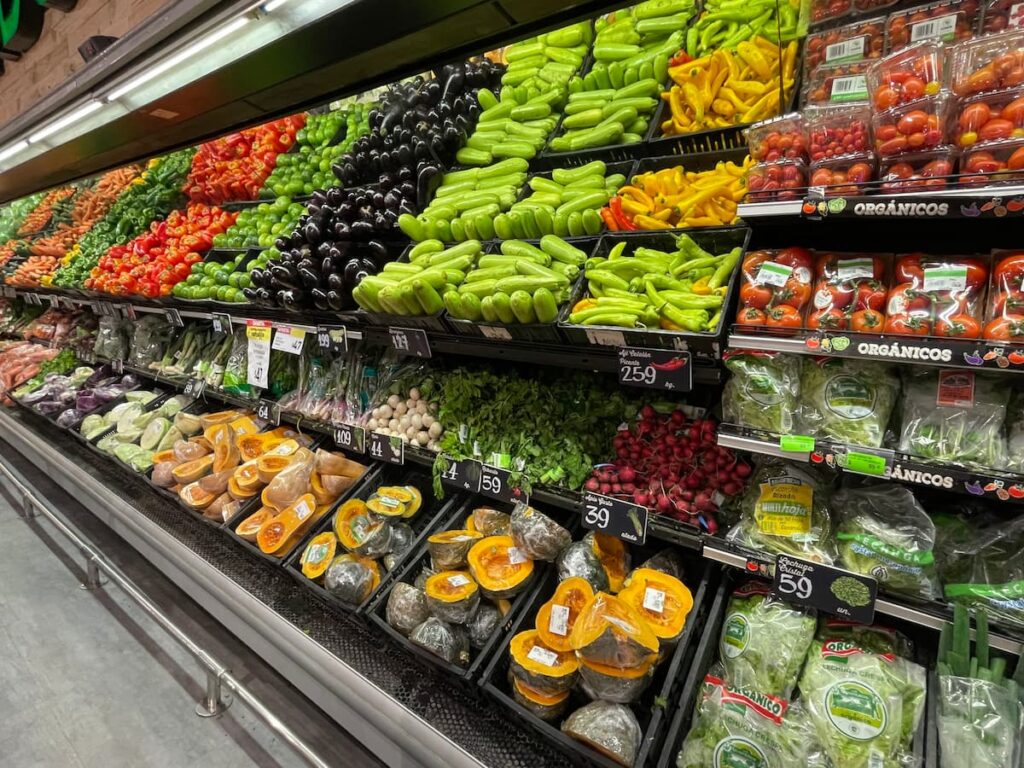 Colorful produce section at a grocery store in Uruguay featuring fresh vegetables like zucchini, eggplant, bell peppers, carrots, squash, and leafy greens, neatly arranged for sale, food quality in uruguay
